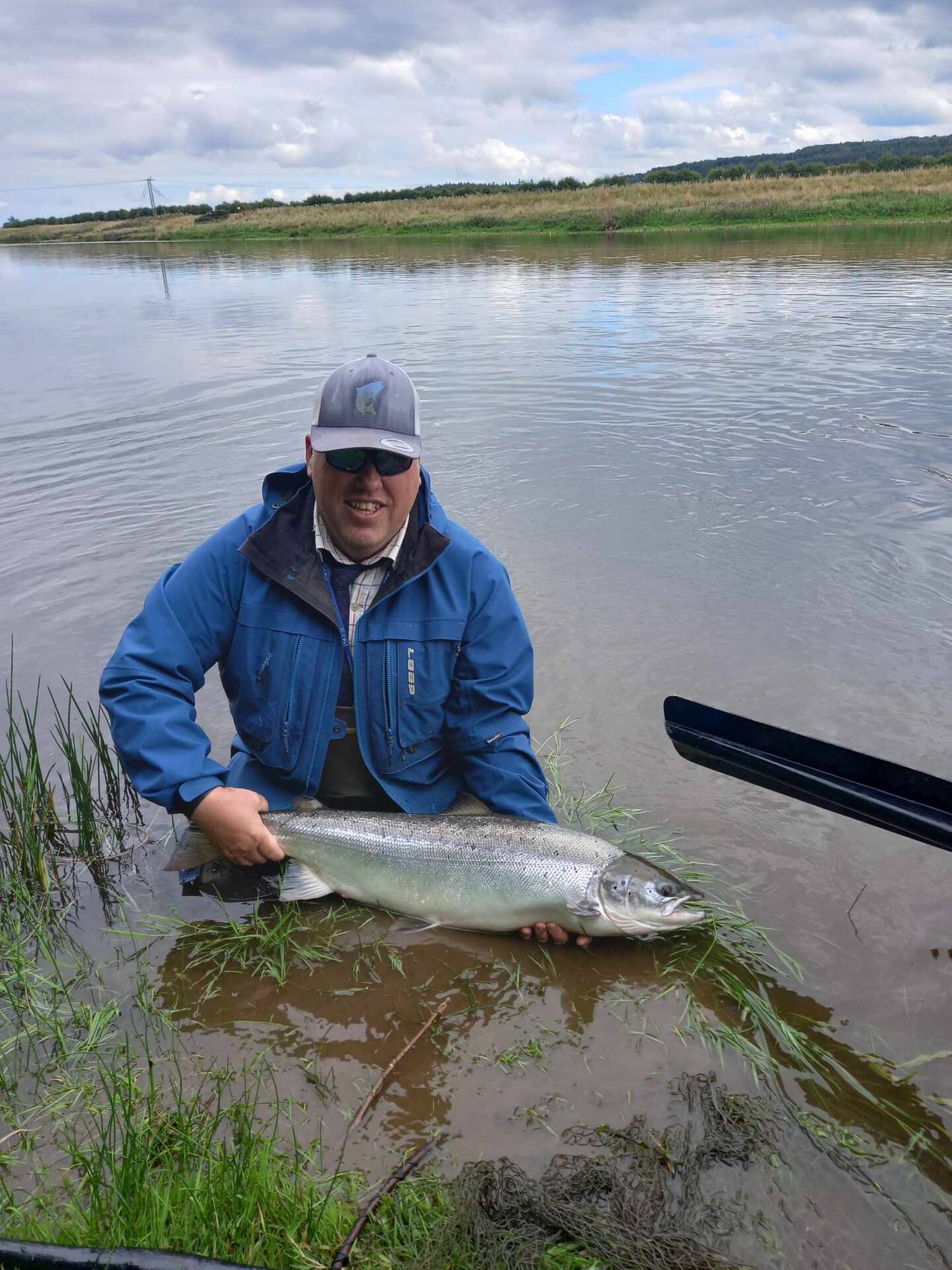 An angler kneeling in the River Tweed holding a salmon in the water