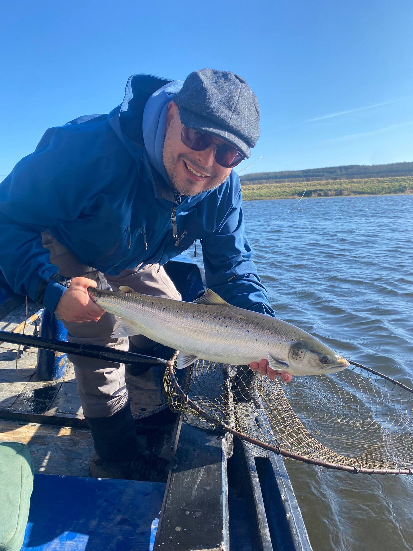 A smiling angler in the boat holding a salmon over the net on a sunny day