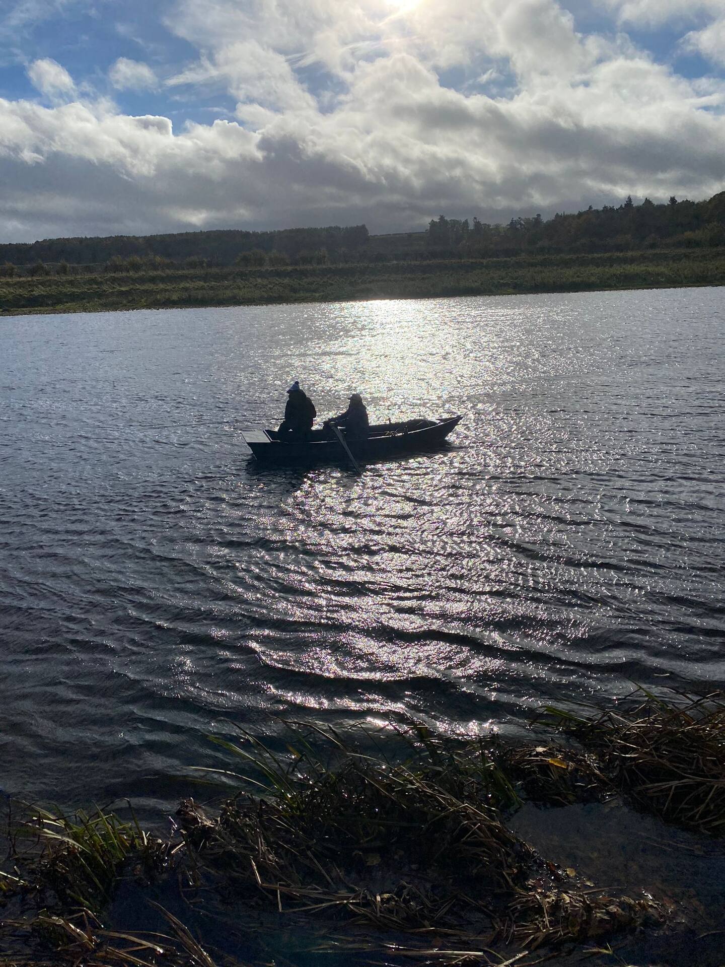 Two anglers in a boat silhouetted against sparkling water on the Tweed