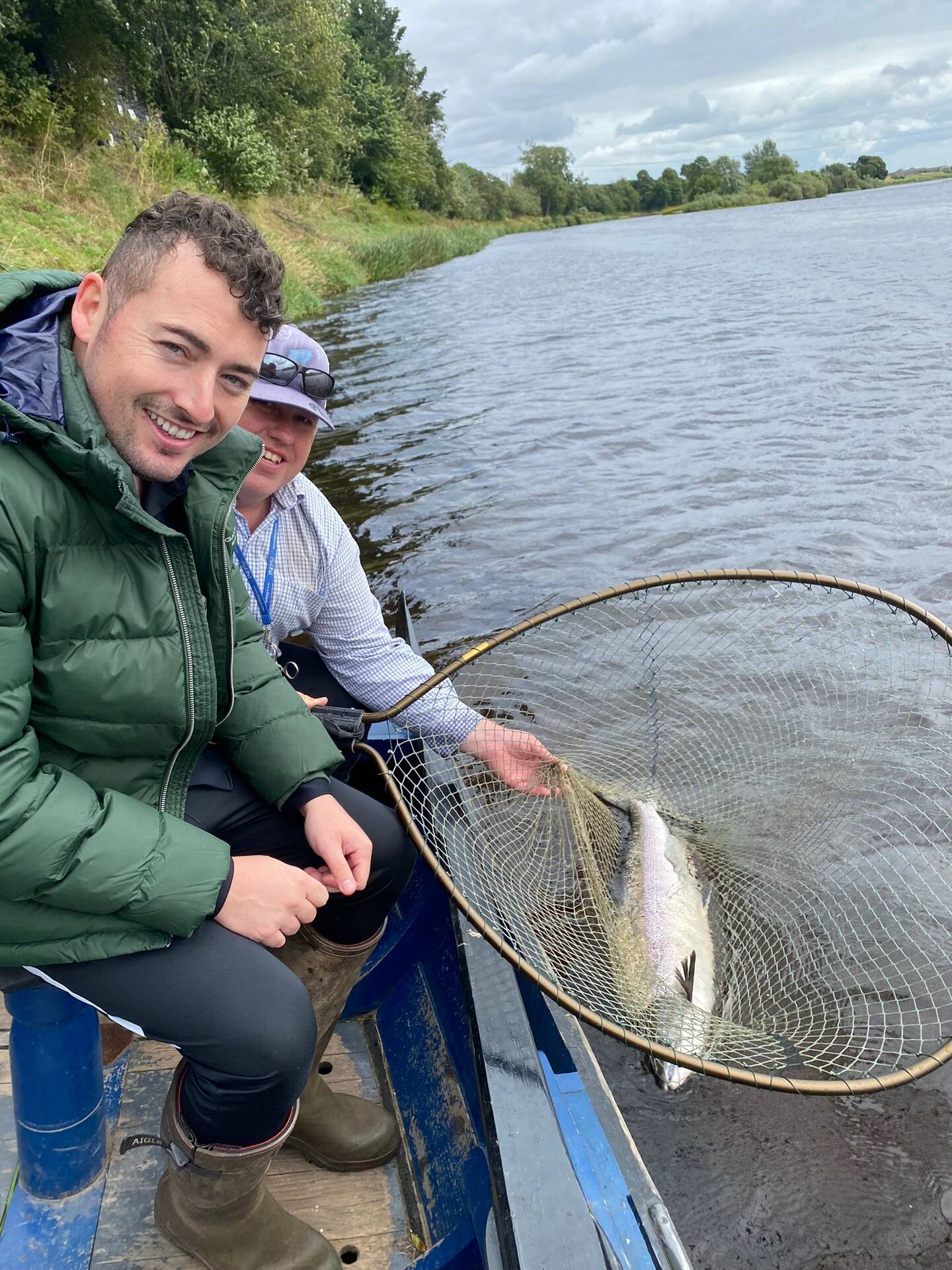 Two smiling anglers in the boat with a salmon in the landing net