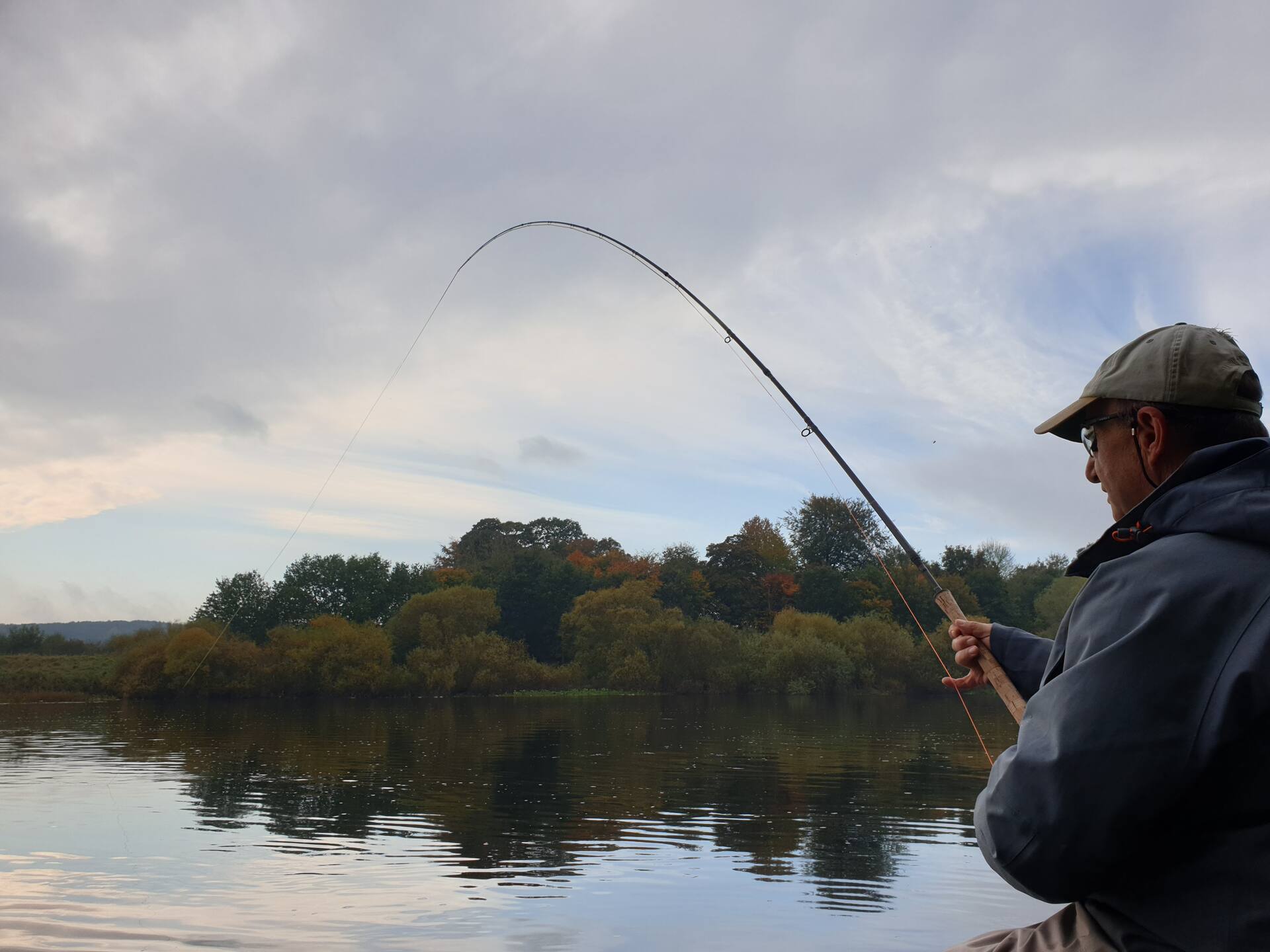 An angler with a bent rod against autumn trees on the River Tweed