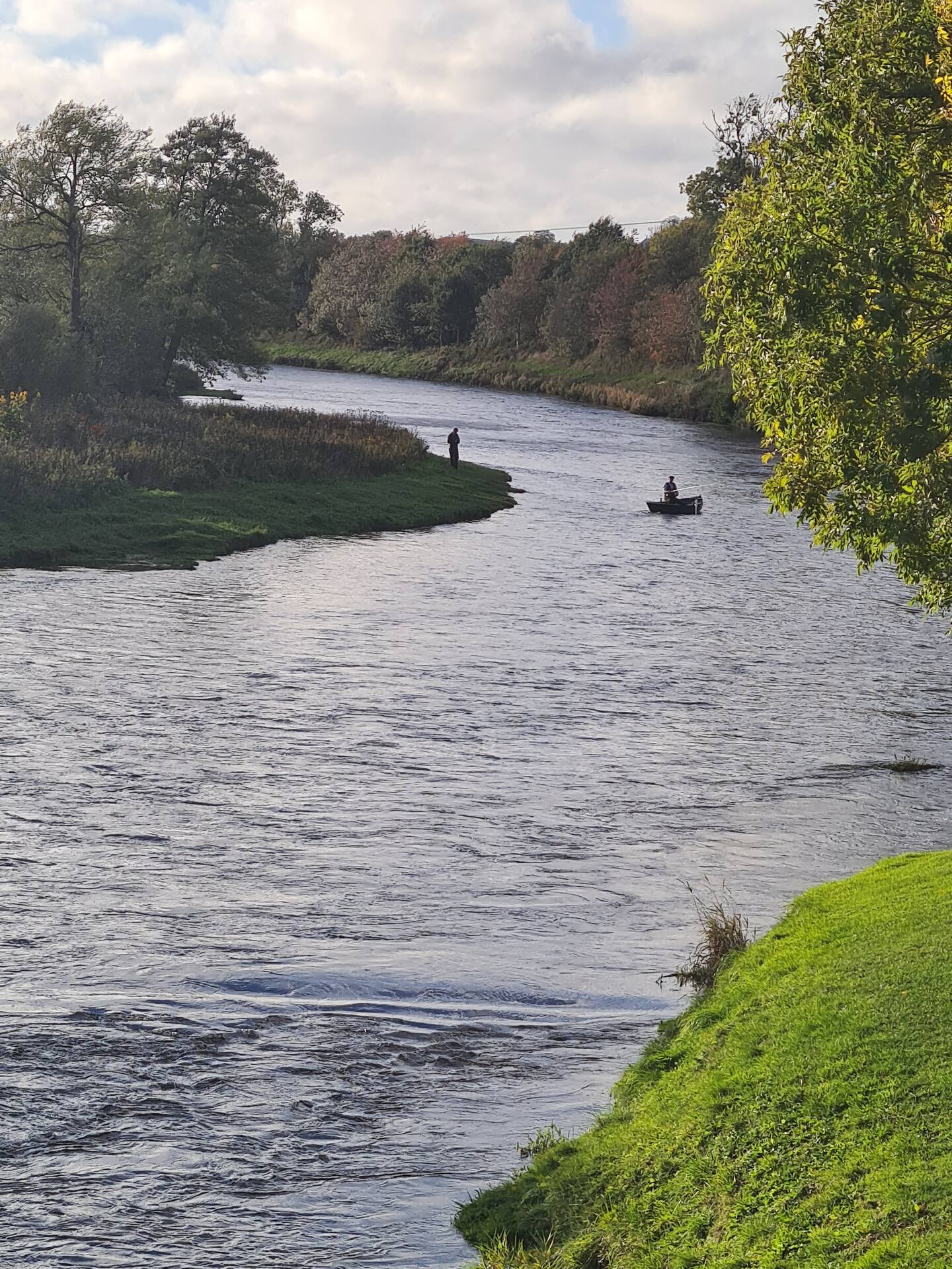 A bank angler and a boat fishing a bend of the River Tweed in autumn
