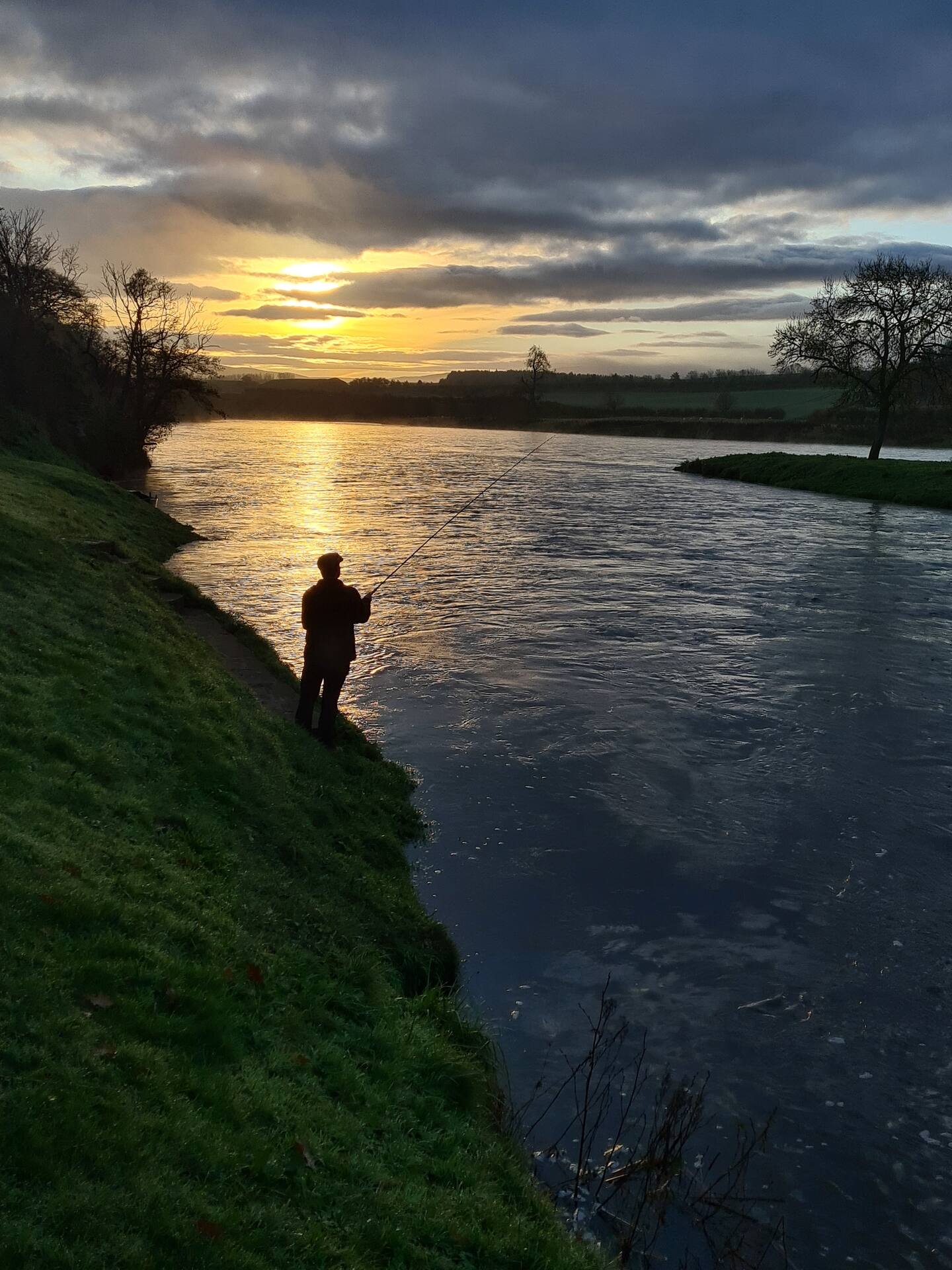 An angler fishing from the grassy bank at sunset on the Tweed