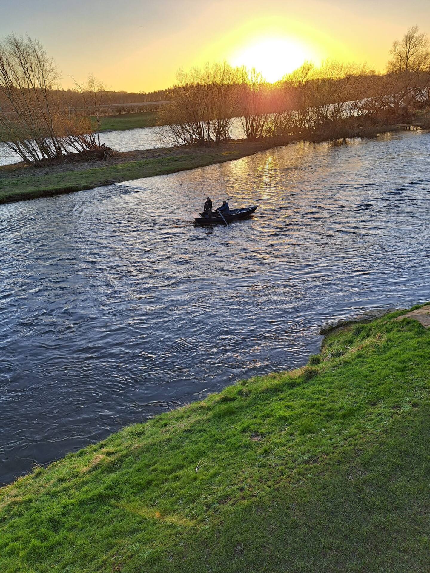 A boat fishing the Tweed at sunset, seen from the high grassy bank