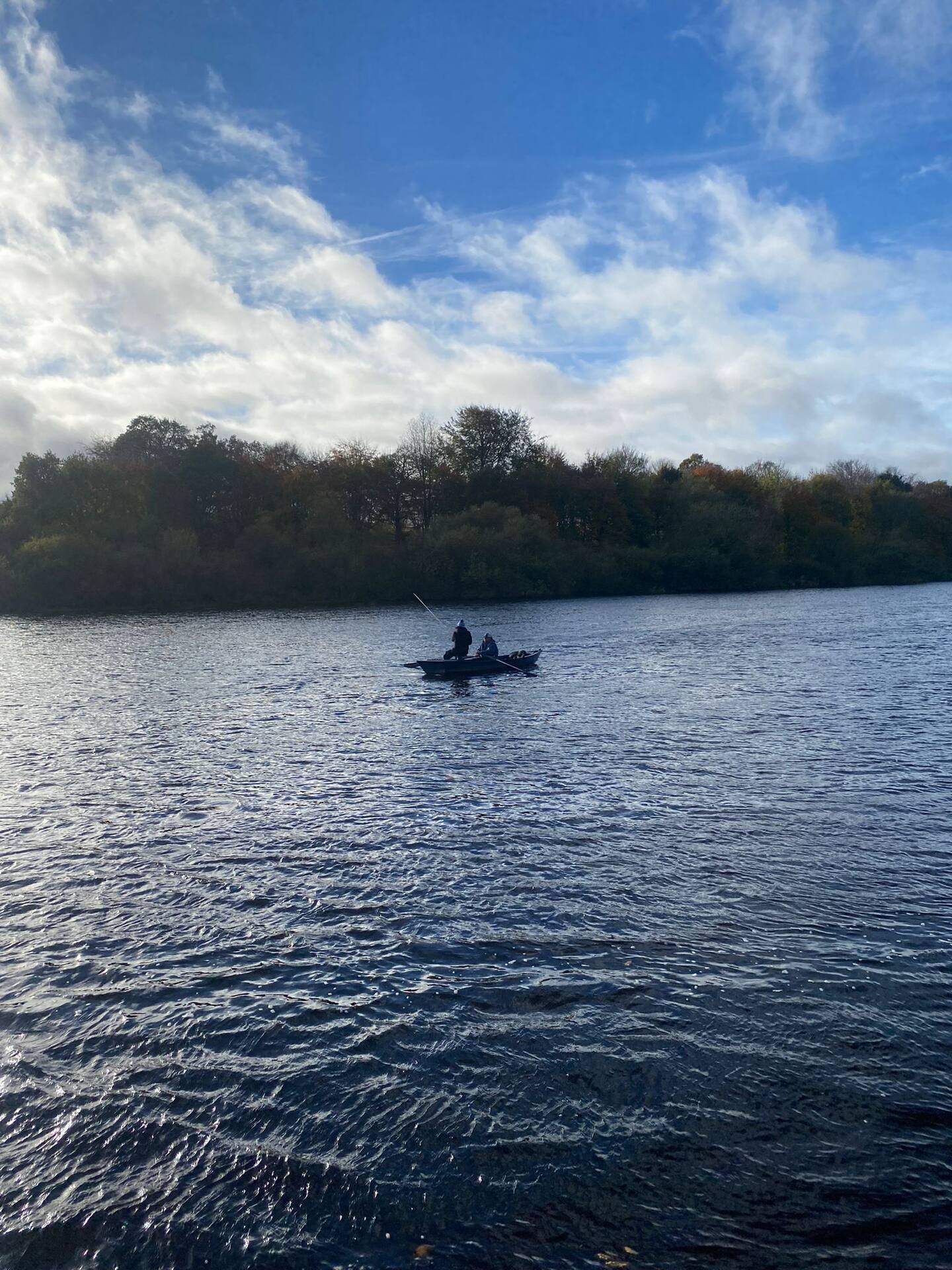 A boat fishing beneath autumn woodland on the River Tweed