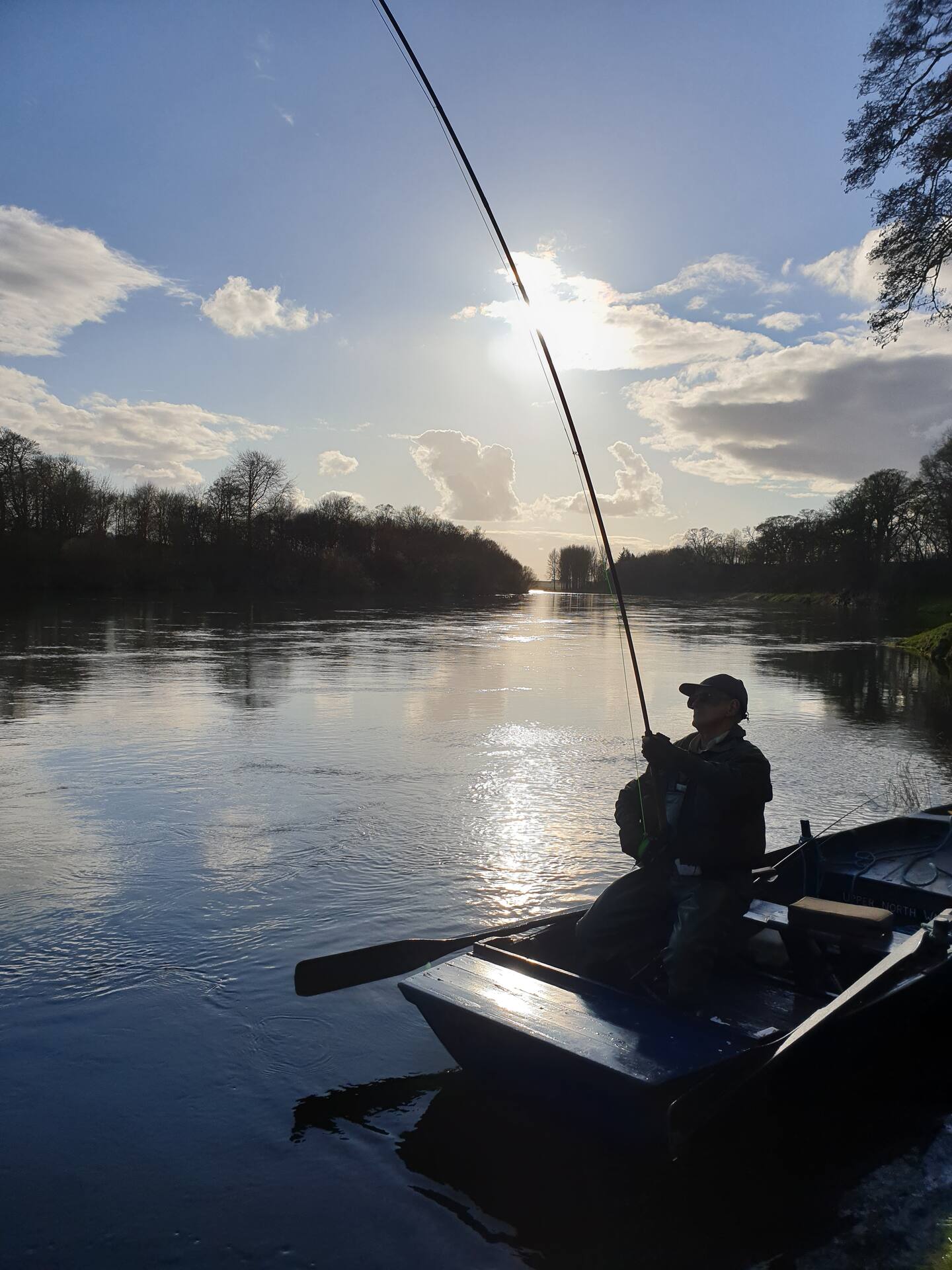 An angler fishing from a boat into low spring sunshine on the River Tweed