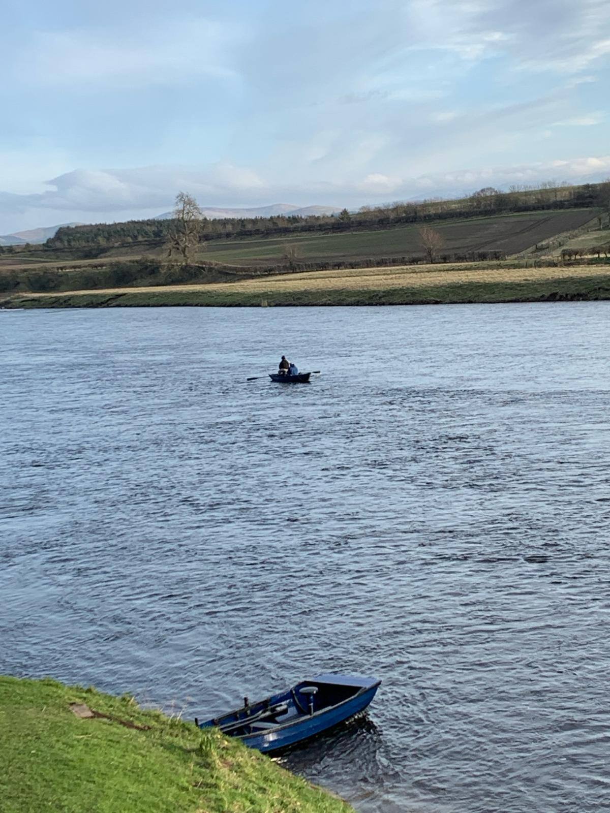 Two boats on the wide River Tweed with fields and hills beyond