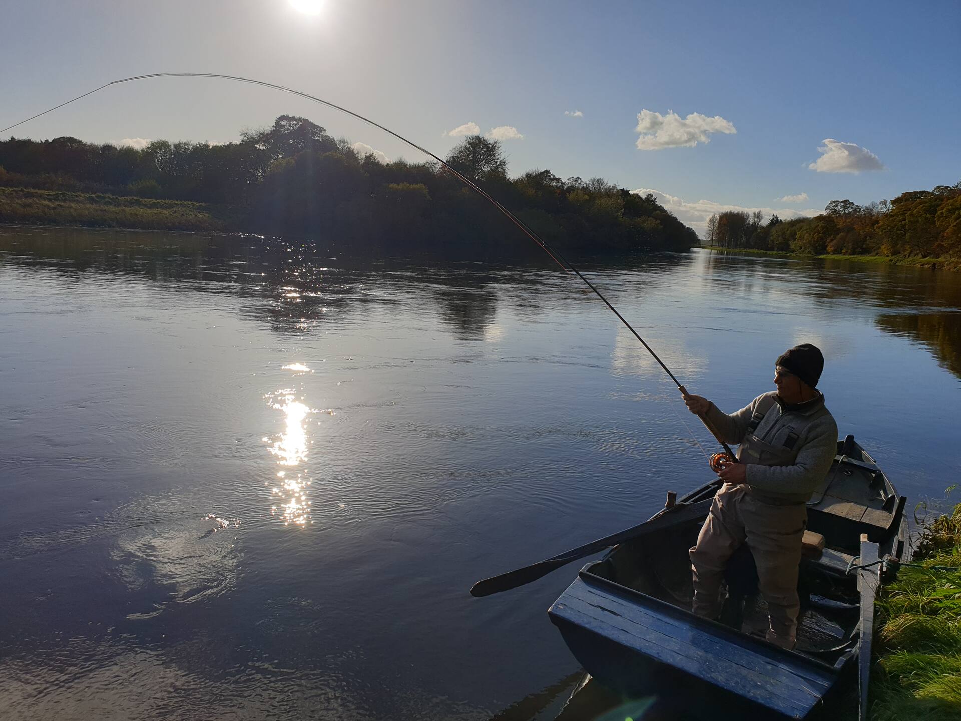 An angler casting from a moored boat on a sunny autumn afternoon on the Tweed