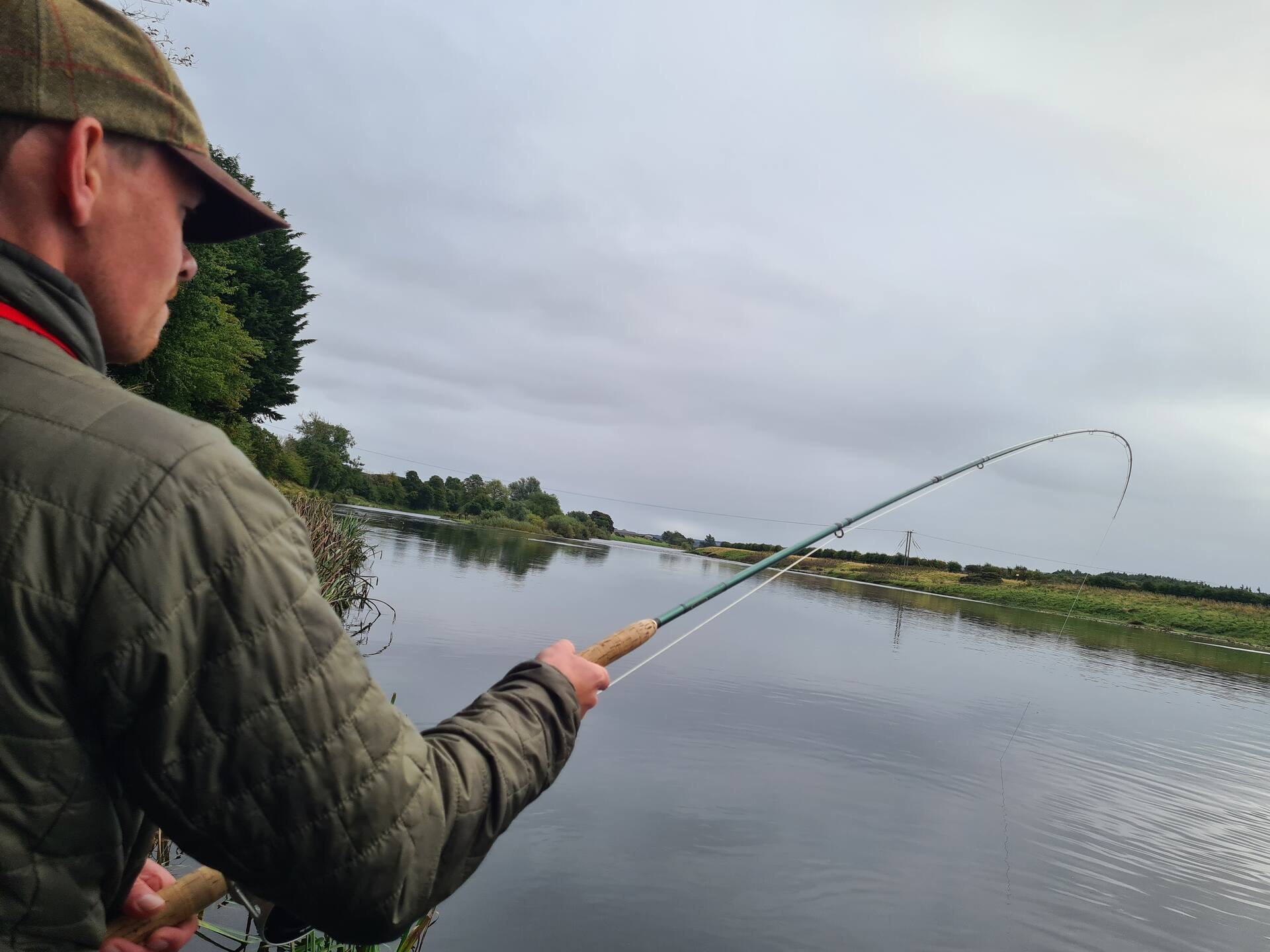 An angler's view of a fly rod bent into a fish on a grey day on the Tweed
