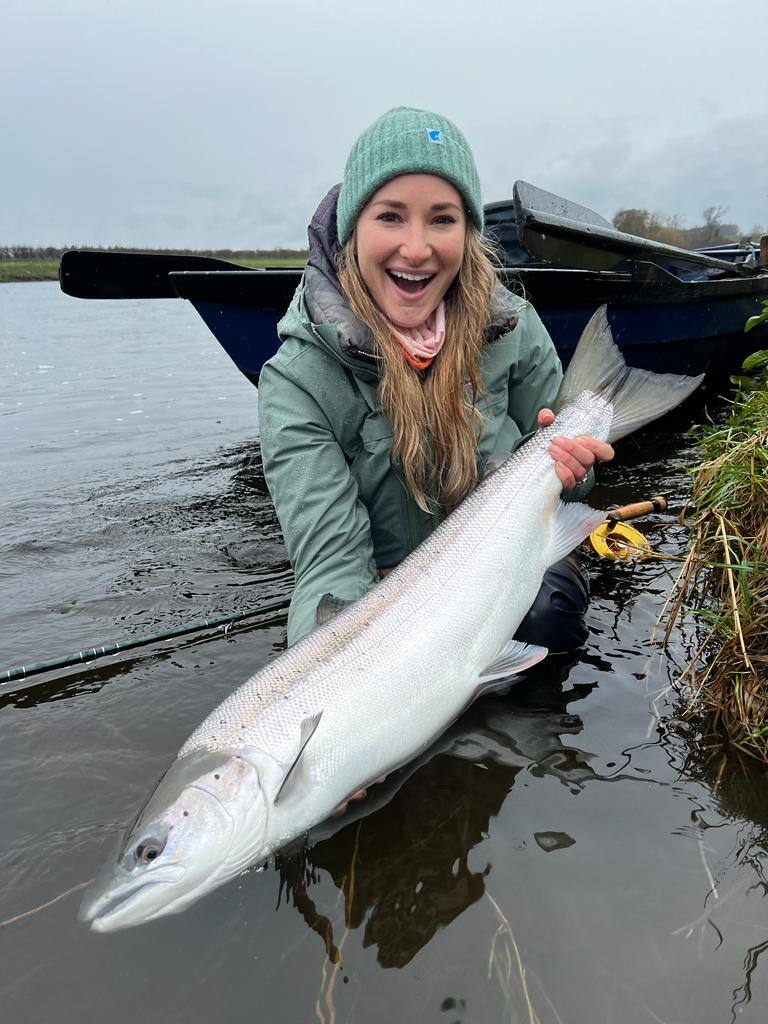 A delighted angler kneeling in the river beside the boat with a fresh silver salmon