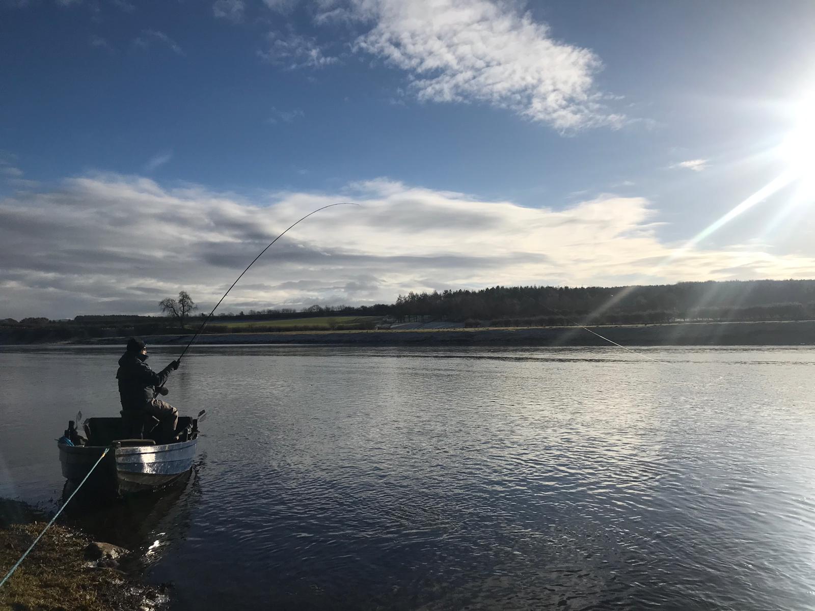 An angler playing a fish from a boat on a bright winter morning