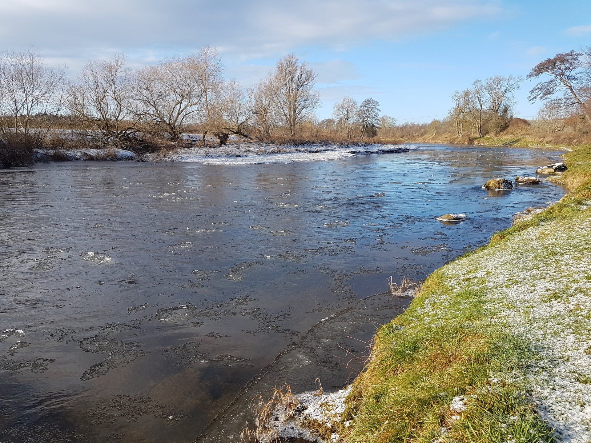 A wide winter view of the River Tweed with ice at the margins