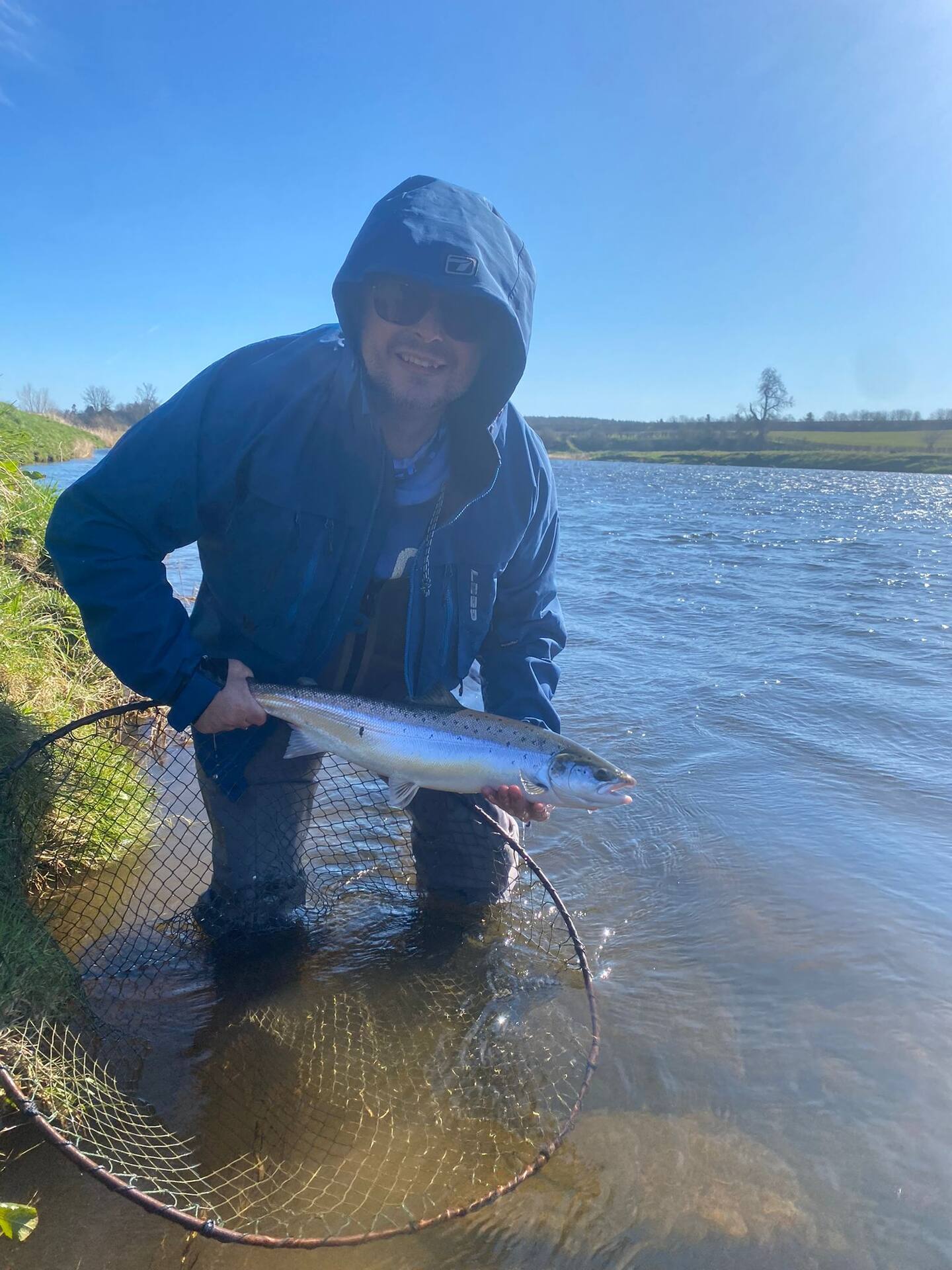 A smiling angler standing in the river with a spring salmon over the net