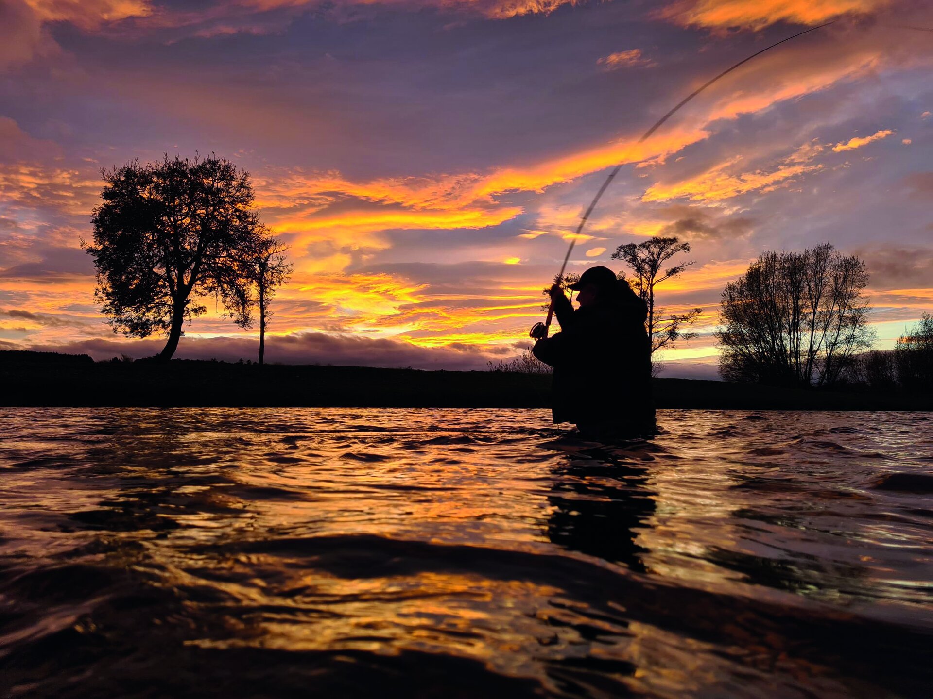 An angler playing a salmon at sunset on the River Tweed