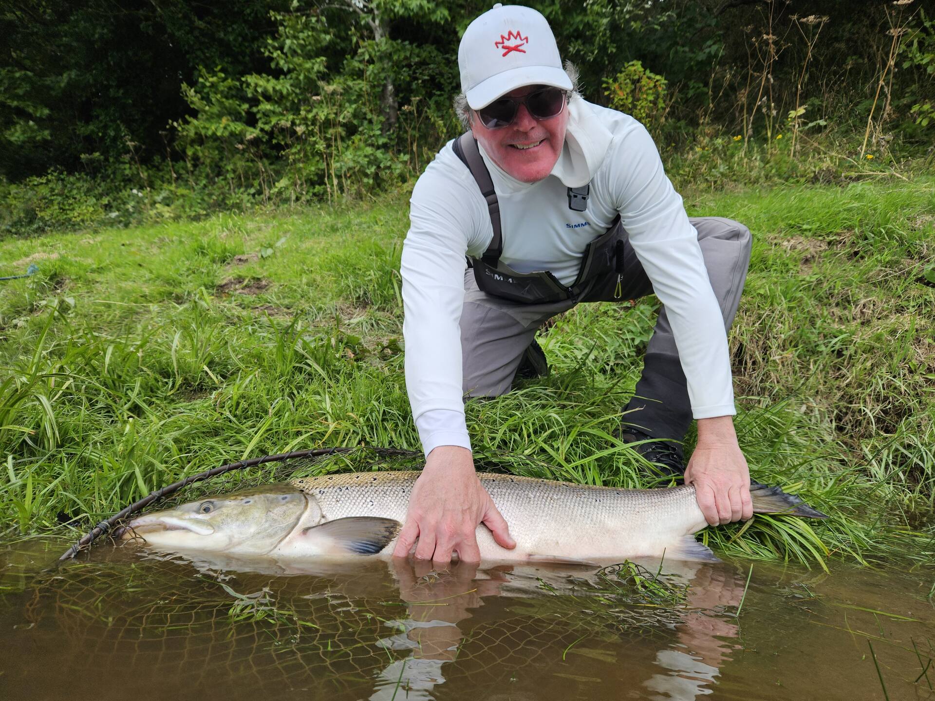 A smiling angler at the water's edge with a big salmon in the net, ready for release