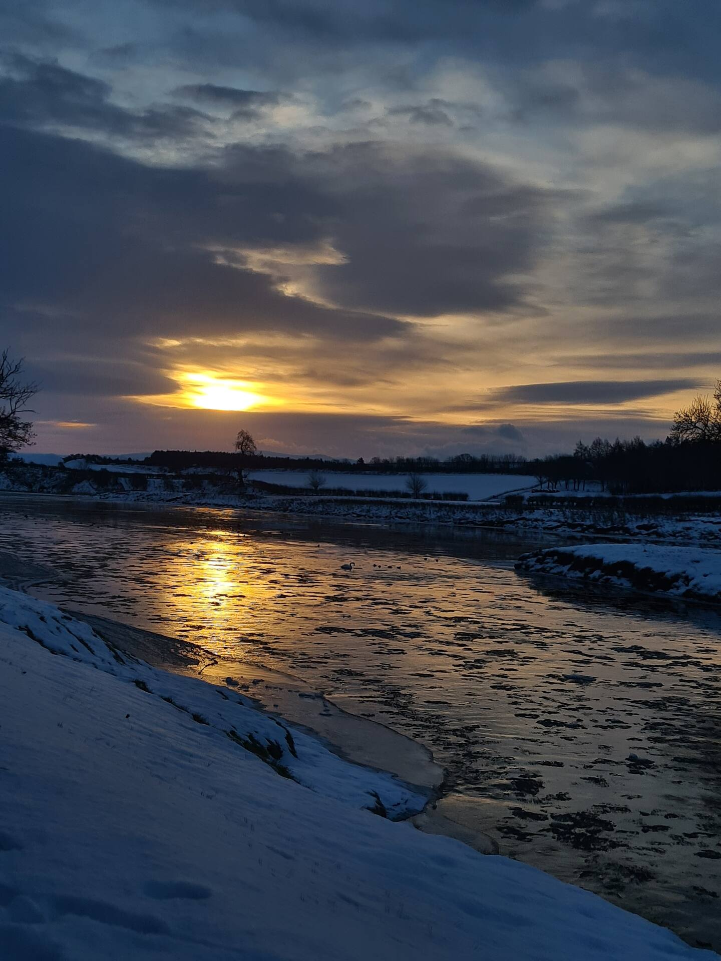 The River Tweed in winter, snow on the banks and ice on the water at sunset