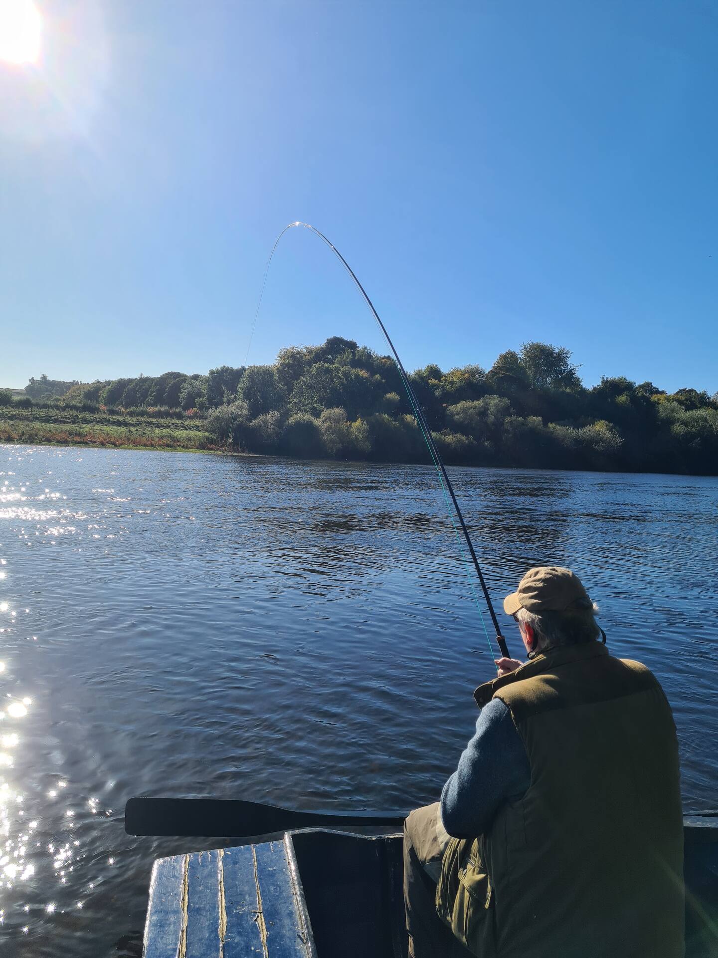 An angler in a boat into a fish on a bright, sunny day on the Tweed